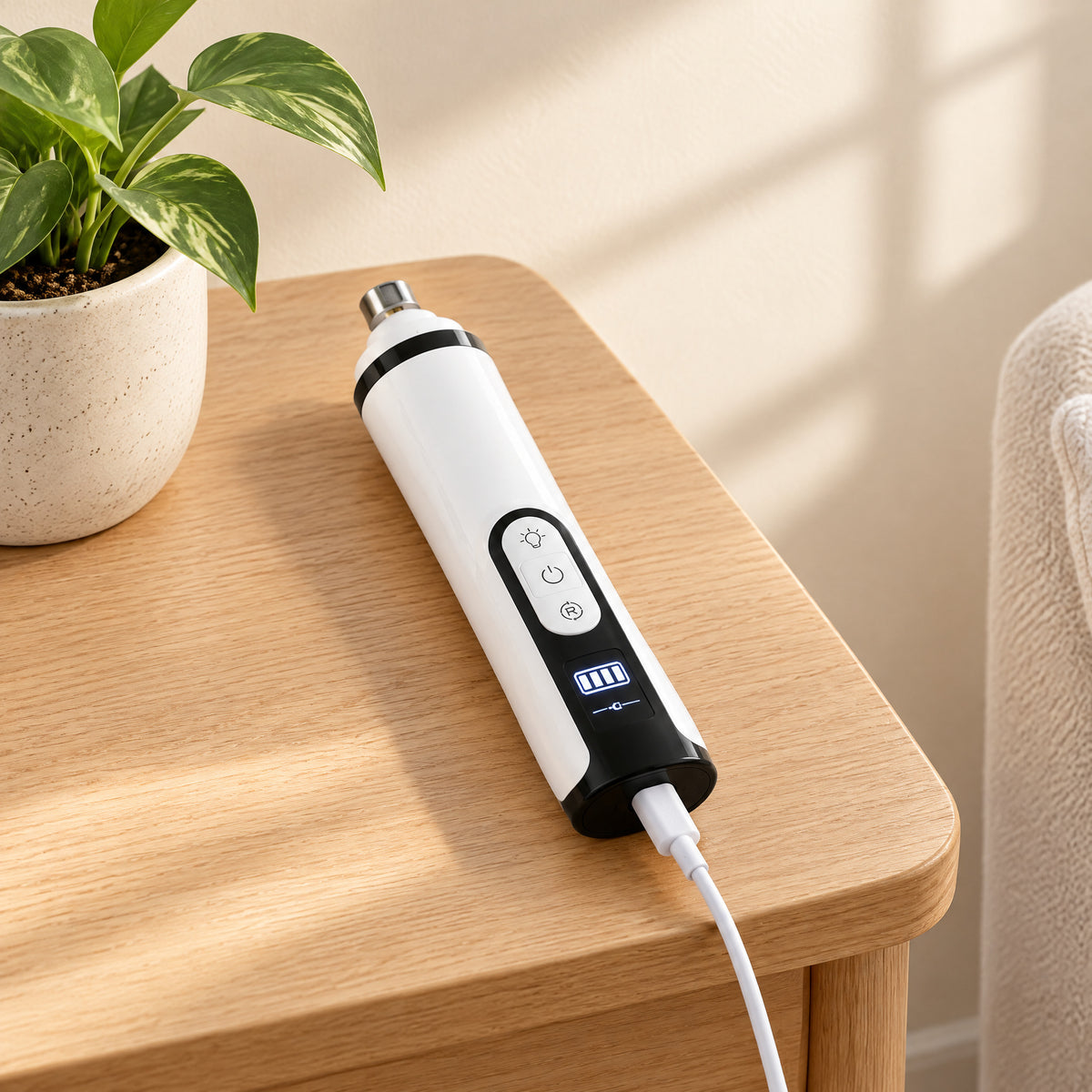 The nail grinder charging with a USB cable on a side table, display showing the battery level