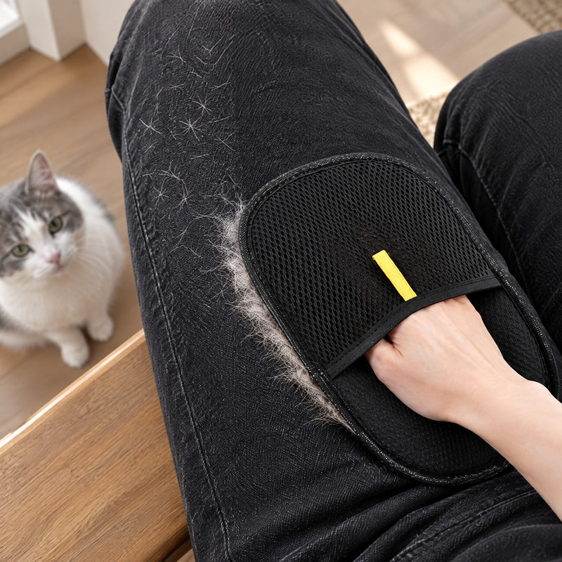 The mitt stroking white cat hair off black jeans while a white and gray cat looks up
